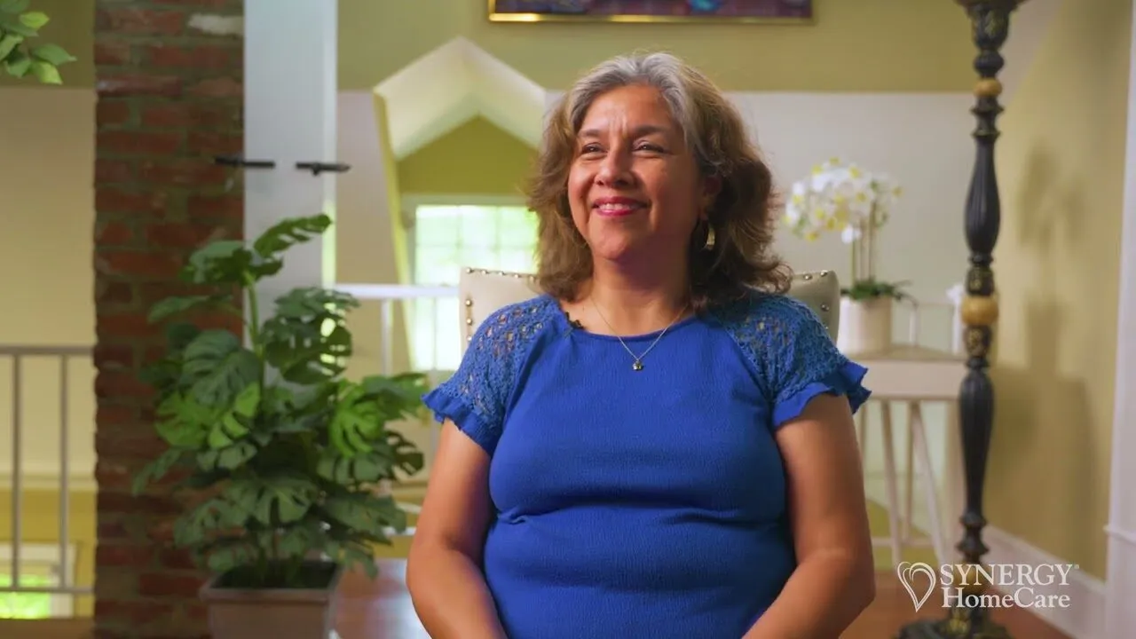A smiling SYNERGY HomeCare client at home, play the video to meet the team