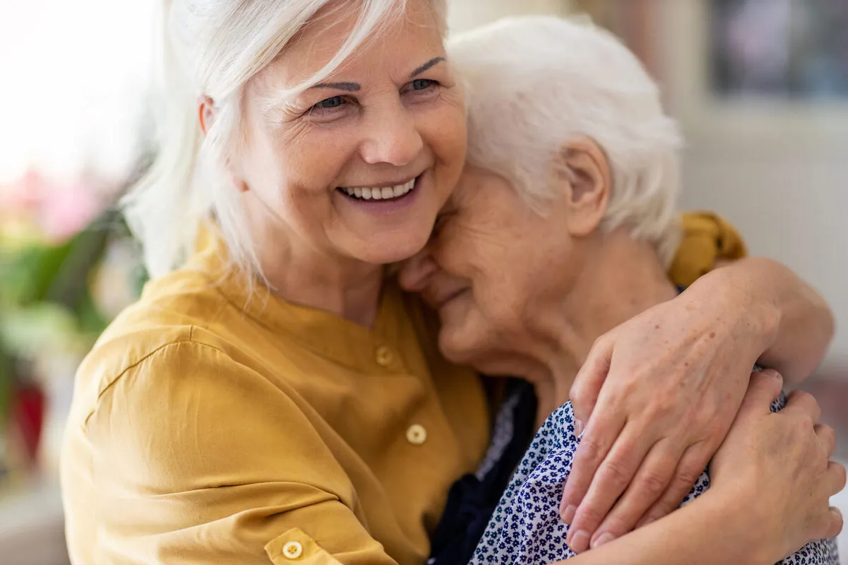 Two women sharing a warm, joyful embrace at home, the genuine connection at the heart of SYNERGY HomeCare
