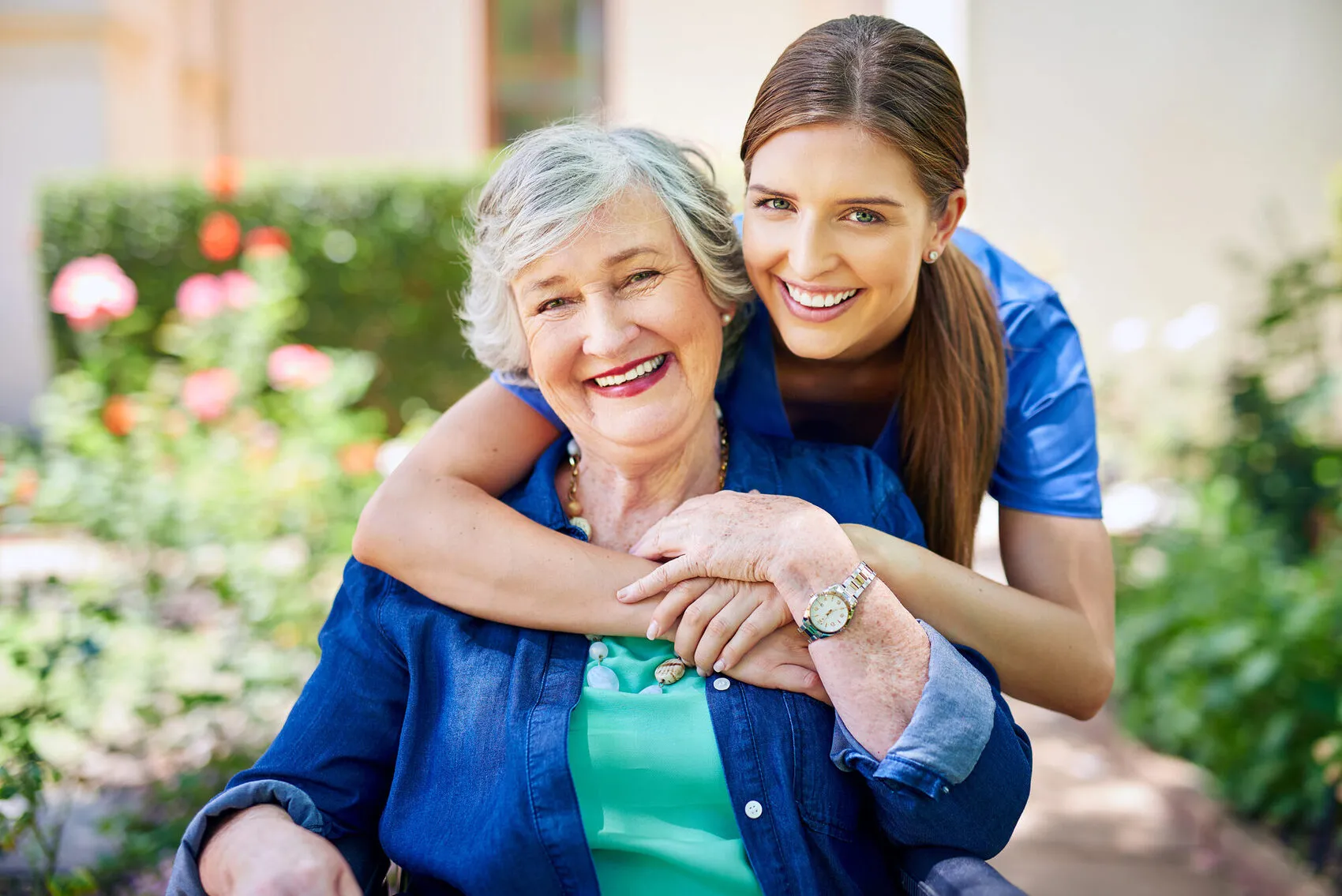 A SYNERGY HomeCare caregiver and a smiling senior woman enjoying a warm moment outdoors in the garden