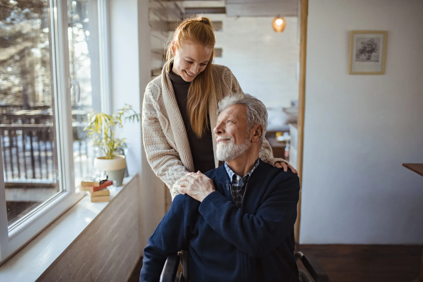 A SYNERGY HomeCare caregiver sitting and talking warmly with a senior man beside a window during a memory-care visit